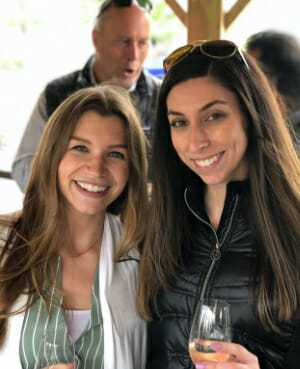 Two employees smiling and holding wine glasses