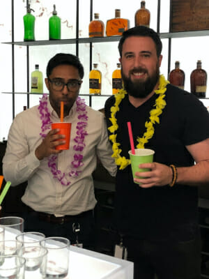 Two employees wearing luau leis and drinking from colorful cups