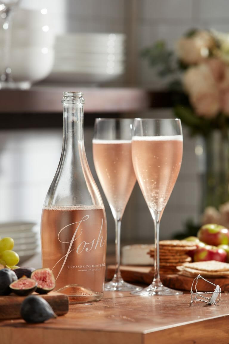 open bottle of josh cellars rose prosecco with full champagne glasses and snack board on table