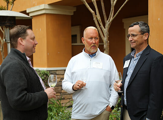 Three men talking and holding wine glasses